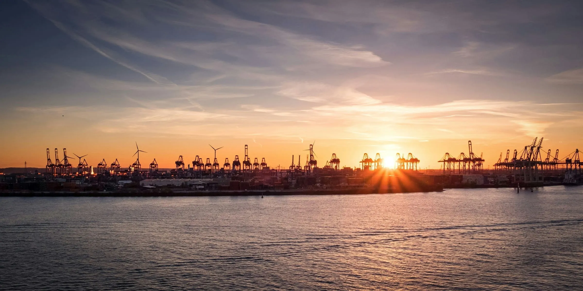 Silhouette eines Boots im Hamburger Hafen bei Sonnenuntergang, warmes Gegenlicht über ruhigem Wasser.